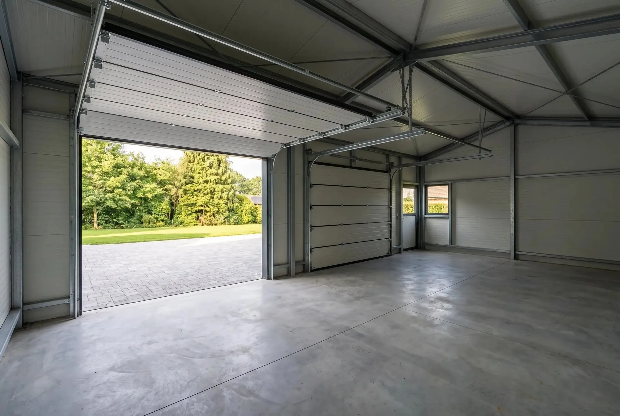 Innenraum der Stahlgarage mit Betonboden und Blick durch das offene Sektionaltor