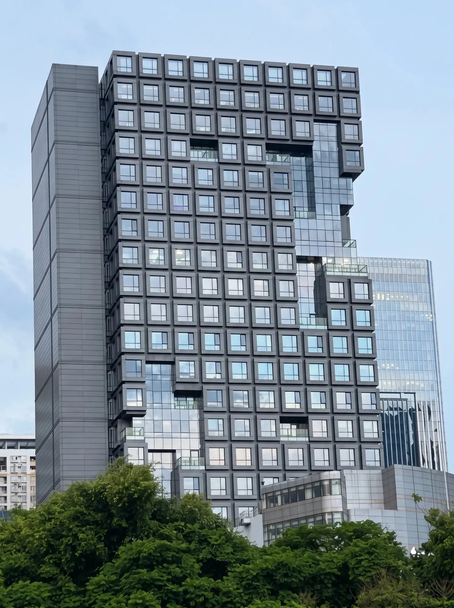 Hochhaus aus gestapelten Raummodulen mit quadratischen Fensterrahmen und verglasten Einschnitten